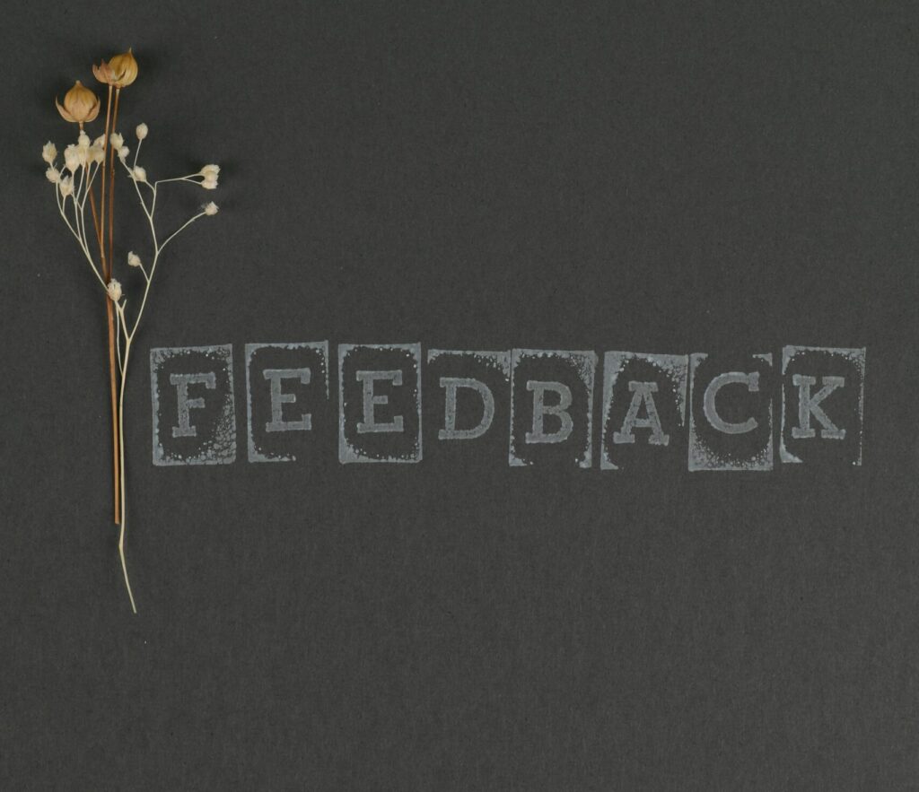 Artistic image of dried flowers on a dark surface featuring the word 'Feedback'.